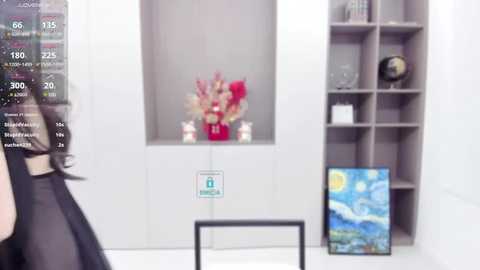 Media: Video of a modern, minimalist room with a white background, featuring a woman in a black top, a red flower arrangement, a globe, and a colorful landscape painting.