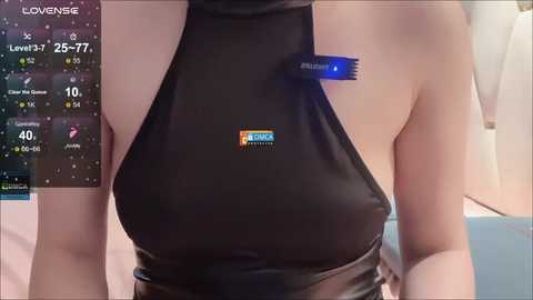 A video of a woman wearing a black, halterneck latex dress with a visible bra and a blue bra clasp. The background shows a smartphone displaying a weather app with a temperature of 25\u00b0C and a humidity of 71%.