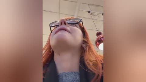 Media: A video of a young woman with fair skin and red hair, wearing glasses, standing indoors with a low angle shot focusing on her upturned face and neck, surrounded by blurred, reddish-brown vertical objects.