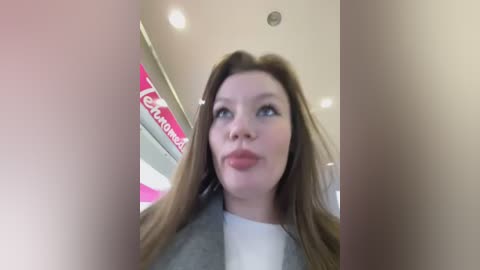 Media: A video of a young woman with long brown hair, light skin, and red lipstick, wearing a white top and gray jacket, standing in a brightly lit convenience store with a \"Circle K\" sign.