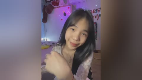 Media: A video of an Asian woman with straight black hair and fair skin, wearing a white blouse, smiling, in a festive, dimly lit room with Christmas decorations.