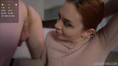 Media: A video of a fair-skinned woman with red hair, wearing a beige sweater, stretching her arms above her head. The background is blurred, featuring a white wall and a window. The image has a watermark.