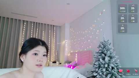 Media: A video shows a young Asian woman with dark hair, wearing minimal makeup, in a modern bedroom with fairy lights, a Christmas tree, and a bed.