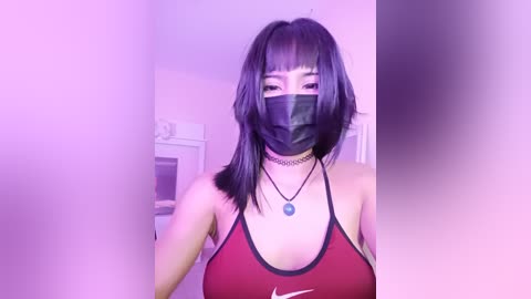 Video of an East Asian woman with straight black hair and a black face mask, wearing a red Nike tank top and black choker. She stands indoors, illuminated by soft purple lighting.