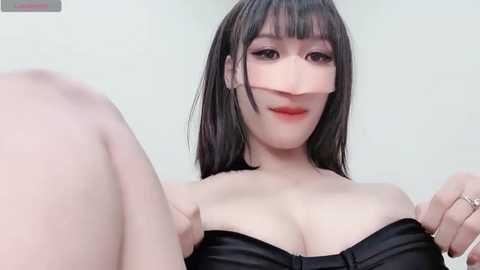 Media: A close-up video of an East Asian woman with straight, black hair and pale skin, wearing a black strapless top, making a playful face.