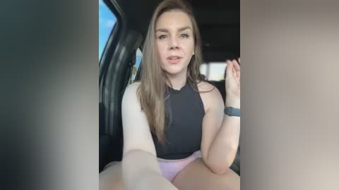 Media: Video of a young woman with long, light brown hair, wearing a black sleeveless top and pink shorts, sitting in a car.