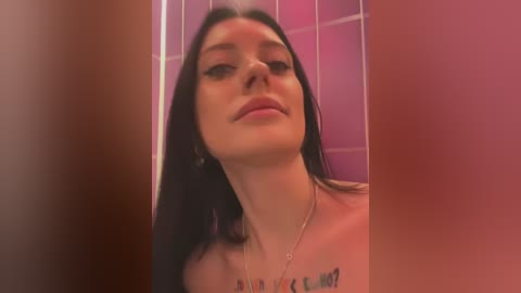 Media: A video of a woman with long black hair, wearing minimal makeup, and a necklace, standing in a tiled shower with a blurred background.