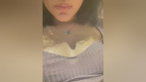 Media: Video of a person's chest and face, wearing a grey ribbed tank top with a large, yellow stain covering the cleavage area. The person has light brown skin and full lips.