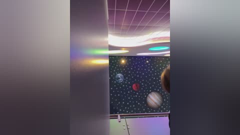 Media: A video of a classroom ceiling adorned with a vibrant, colorful space-themed mural featuring planets and stars, set against a backdrop of modern, fluorescent lighting.