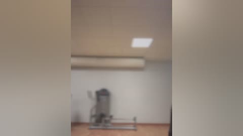 Media: A blurred video of a gym with a wall-mounted fan, an elliptical machine, and a ceiling-mounted air conditioner. The room has beige walls and wooden flooring.