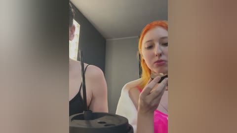 Media: A video shows a young woman with orange hair and a white top, applying lipstick in a dimly lit bathroom. Her reflection is visible in a mirror, revealing her bare shoulder and a black bra strap.