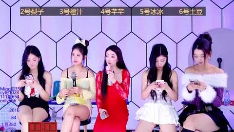 Media: Video of five Asian women in various colorful dresses seated in a row, attentively using smartphones, against a hexagonal patterned backdrop.