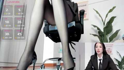 Media: A video of a woman in a black business suit, sitting in a chair with her legs crossed, wearing sheer black pantyhose. A calendar and a potted plant are in the background.