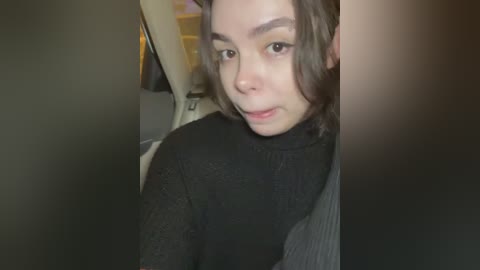 Media: A video of a young woman with light skin and dark hair, wearing a black turtleneck, taken from the car's backseat, showing her slightly tilted head and direct gaze.