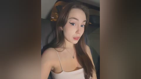 Media: Video of a young woman with long brown hair, wearing a spaghetti strap top, sitting in a car.