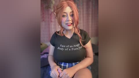 Media: A video of a young woman with fair skin, pink hair, and a smile, wearing a black t-shirt with \"Face of an Angel Body of a Pornstar\" and a blue plaid skirt. She sits in a room with pink walls and a bed in the background.