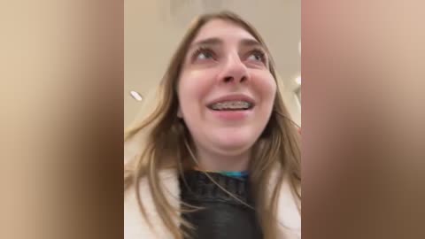 Media: Video of a smiling young woman with straight brown hair, wearing a black shirt, and braces, captured from a low angle.