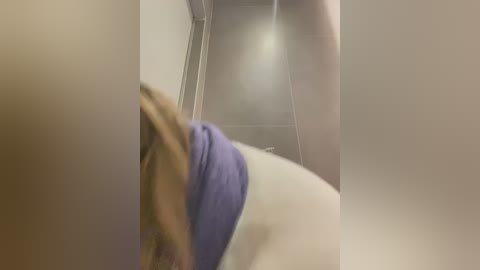 Media: Video of a person's lower body, wearing a blue towel, in a dimly lit bathroom with a white ceiling and beige walls. The image is slightly blurred and out of focus.