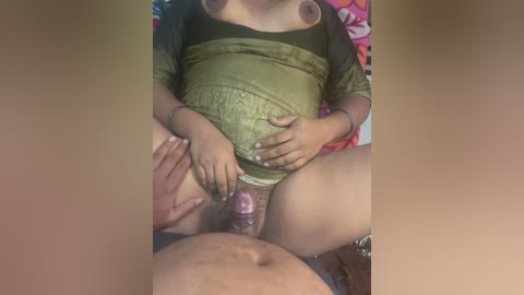 Media: Video of a pregnant woman in a green lace top, sitting on a bed with a partially visible man's erect penis in her vagina.