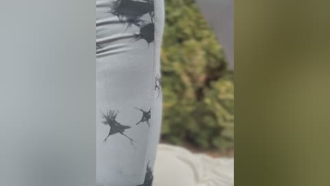 Media: Video of a person's leg clad in white leggings adorned with black, stylized bird silhouettes. Background shows blurred greenery and a beige wall.