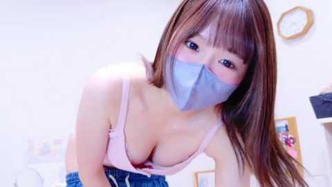 Media: A video of an Asian woman with light skin, brown hair, wearing a pink bra and blue shorts, with a gray duct tape over her mouth, taken indoors.