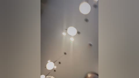 Media: Video of a dimly lit interior with a string of white, glowing orbs dangling from the ceiling, creating a soft, ambient atmosphere. The background is soft, neutral tones, and the lighting is gentle and warm, giving a cozy, intimate feel.