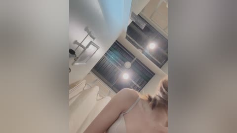 Media: Video of a woman in a white tank top, seen from behind, standing in a modern bathroom with a white countertop, silver faucet, and a towel rack.