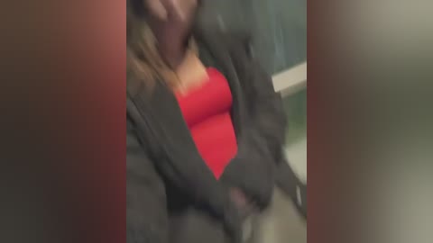 Media: Blurry video of a woman in a red tank top and gray jacket, with a blurred background. The image is out of focus.