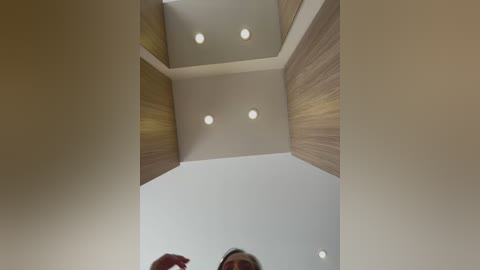 Media: Video of a modern, light-filled ceiling with recessed lights and wooden paneling, viewed from below. The ceiling features a geometric design with clean lines and soft lighting, creating a minimalist aesthetic.