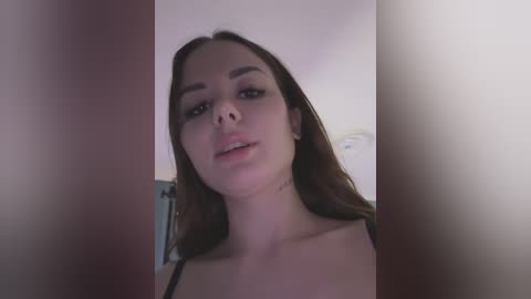 Media: Video of a young woman with light skin, straight brown hair, and dark eyebrows. She wears a black spaghetti-strap top, with a neutral background and soft lighting.