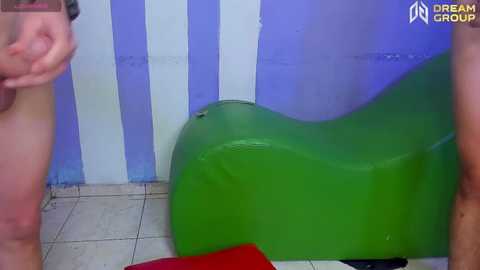 Media: A video of a green, cushioned chair with a person's bare arm and hand on the left side, against a purple and white striped wall.