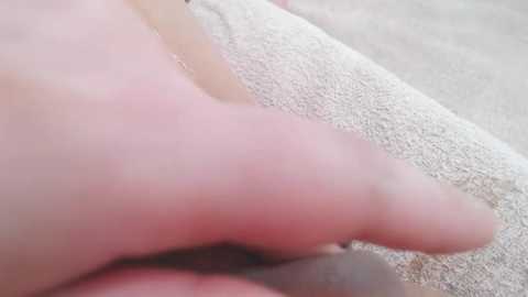 Media: Close-up video of a Caucasian male's pinkish, slightly swollen left hand, with a pale, textured white towel draped across the background. The hand's fingers are slightly bent, and the skin appears slightly reddened.