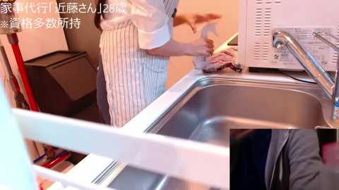 Media: Video of a person in a white apron cleaning a stainless steel sink with a sponge in a modern kitchen. Text in Japanese overlaid.