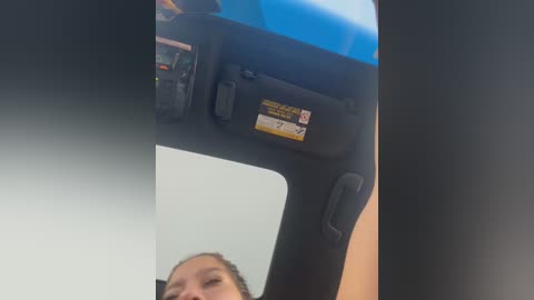 Media: Video of a young person, likely female, with light brown skin and brown hair, looking through a car's side mirror, showcasing the car's interior with a blue lighted screen and various control buttons.