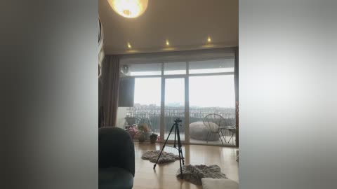 A video of a modern, minimalist living room with a glass balcony door, a black tripod, and a plush white chair. The room is bright and airy with a wooden floor and soft lighting.