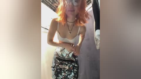 Media: Video of a slender, fair-skinned woman with red hair, wearing a white lace bra and floral-patterned skirt, standing in a dimly lit, narrow hallway with exposed brick ceiling.