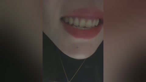 Media: A close-up video of a woman's face, showing a wide smile with visible teeth, red lipstick, and a small mole on her cheek. She wears a black top and a thin gold necklace.