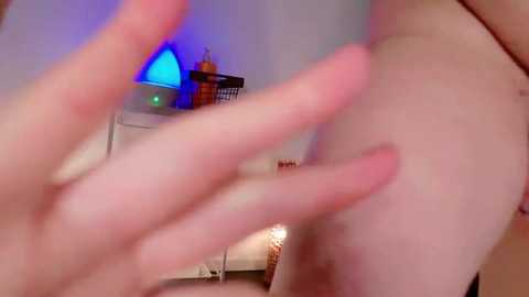 Media: A blurry, close-up video of a person's hand touching their bare buttocks, with a background featuring a blue-lit room with a wicker basket and a small table.