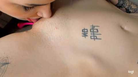 Media: Video of a close-up of a fair-skinned person with a tattoo of Chinese characters on their chest, being kissed by someone with pink lipstick.