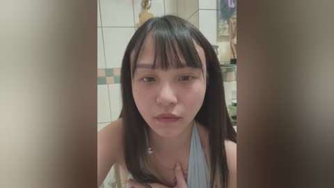 Media: A video of an Asian woman with straight, shoulder-length black hair and bangs, wearing a light blue halter top, in a bathroom with tiled walls and a bathtub.