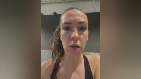 Media: Video of a Caucasian woman with light skin and a ponytail, wearing a black sports bra, indoors with a gym backdrop, showing a bruised and swollen face.