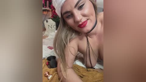 Media: Video of a fair-skinned, blonde woman with red lipstick, wearing a white headband and black choker, lying on a bed with beige blanket, surrounded by festive decorations and a \"NO\" sign.