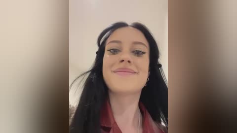 Media: Video of a young woman with long black hair, fair skin, and pink lips, wearing a red leather jacket. She has dark eyeliner and mascara, and is smiling.