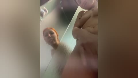 Media: A video shows a naked woman with light skin and red hair, partially obscured by a mirror, her breasts and stomach visible.