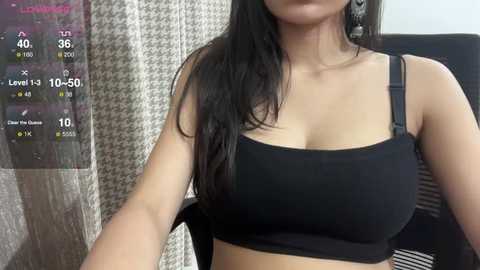 Media: Video of a woman with long, straight black hair, wearing a black, strapless crop top, taken indoors with a houndstooth-patterned curtain and a digital display showing 10% humidity.