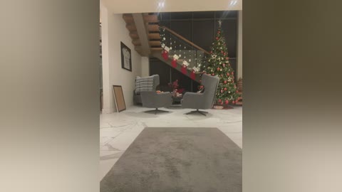 Video of a modern living room with a plush gray rug, gray armchairs, and a decorated Christmas tree, set against a marble floor and wooden staircase.