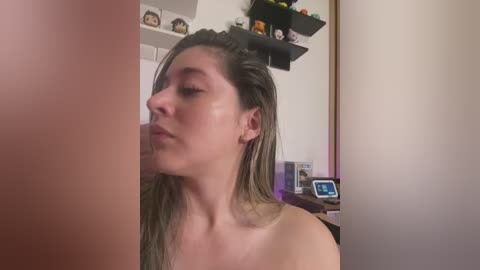 Media: A video of a topless young woman with wet, shoulder-length hair, standing in a bedroom. The background features shelves with figurines, a TV, and a mirror.