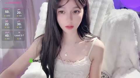 Media: A video of an East Asian woman with long black hair, fair skin, and a petite build, wearing a white lace camisole. She's seated on a plush white bed.