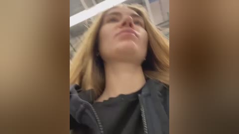 A blurred video of a young woman with fair skin and long blonde hair, wearing a black jacket, captured from a low angle, with indistinct background.