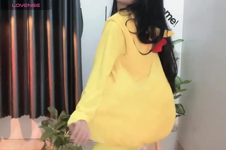 Media: Video of a pregnant woman with long black hair, wearing a yellow dress, standing in front of a window with black curtains.